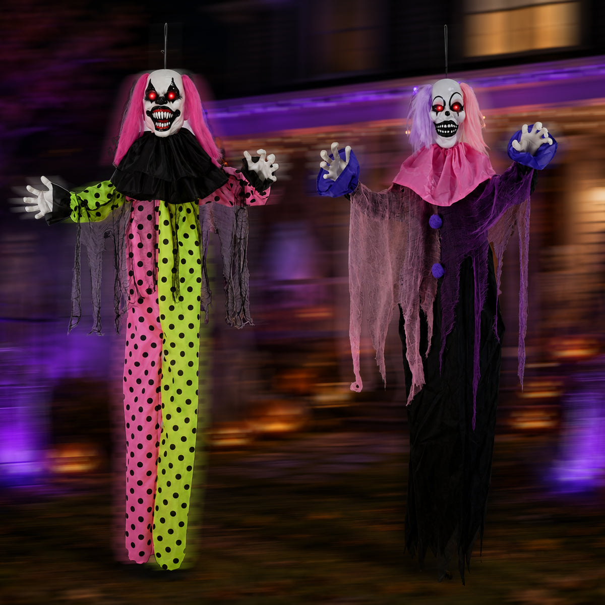Two hanging Halloween clown decorations with spooky painted faces, black ruffled collars, and dramatic colorful outfits. One clown wears a pink and neon yellow polka-dot costume with blue gloves, and the other wears a dark purple and black costume with pink gloves.