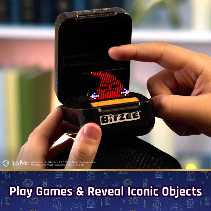 Hand holding a small electronic device labeled 'BITZEE' with a digital display, against a blurred indoor background.