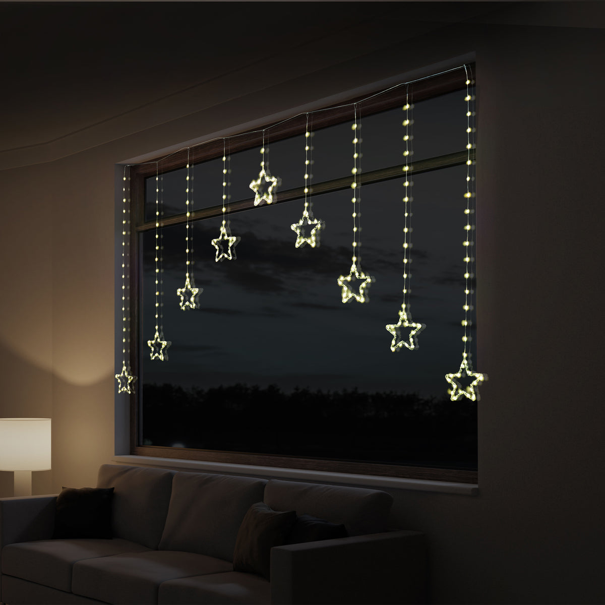 Warm white star-shaped curtain string lights hanging from a window in a dimly lit living room at night.