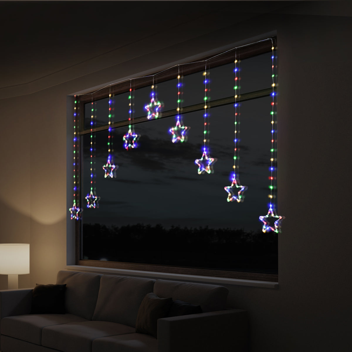 Multicolor LED star curtain string lights hanging from a window in a dimly lit living room at night.