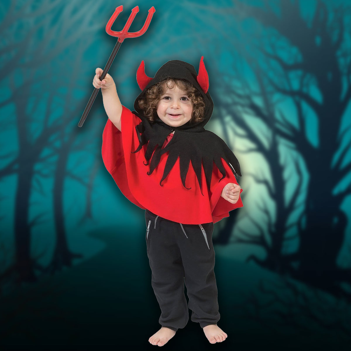 A child wearing a devil costume stands barefoot in a spooky forest setting, holding a red pitch. The costume includes a red cape with black jagged trim, a black hood with red devil horns, and black pants.