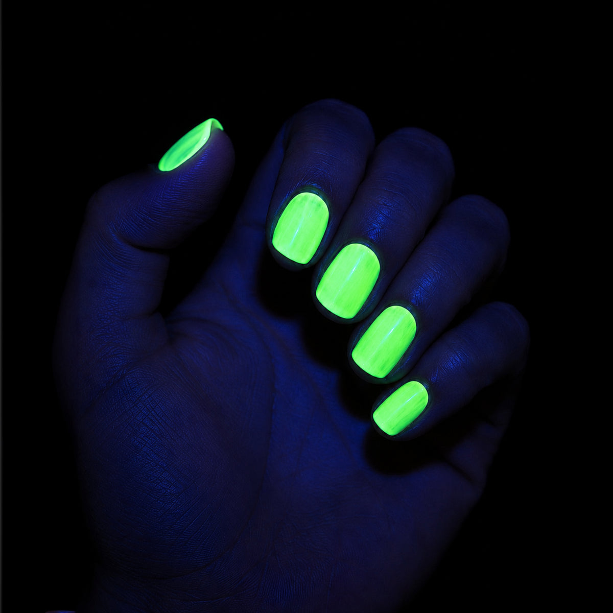 A hand with glowing neon green nail polish under blacklight, shown against a dark black background.