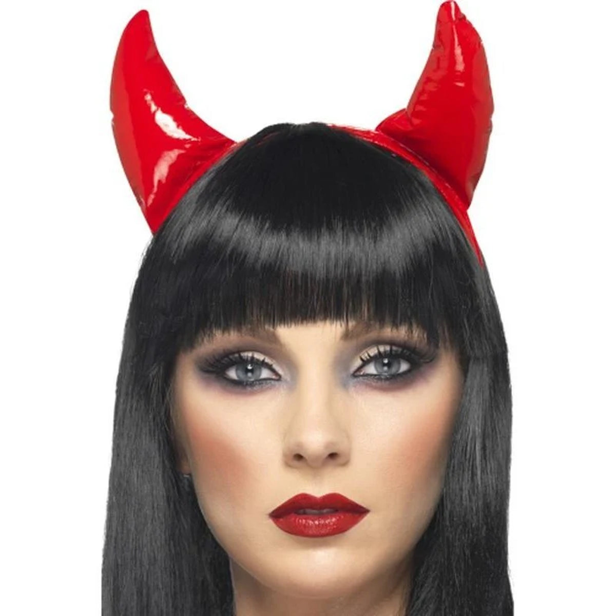 A close-up of a model wearing a glossy red devil horn headband with long black hair, dramatic eye makeup, and red lipstick against a plain white background.