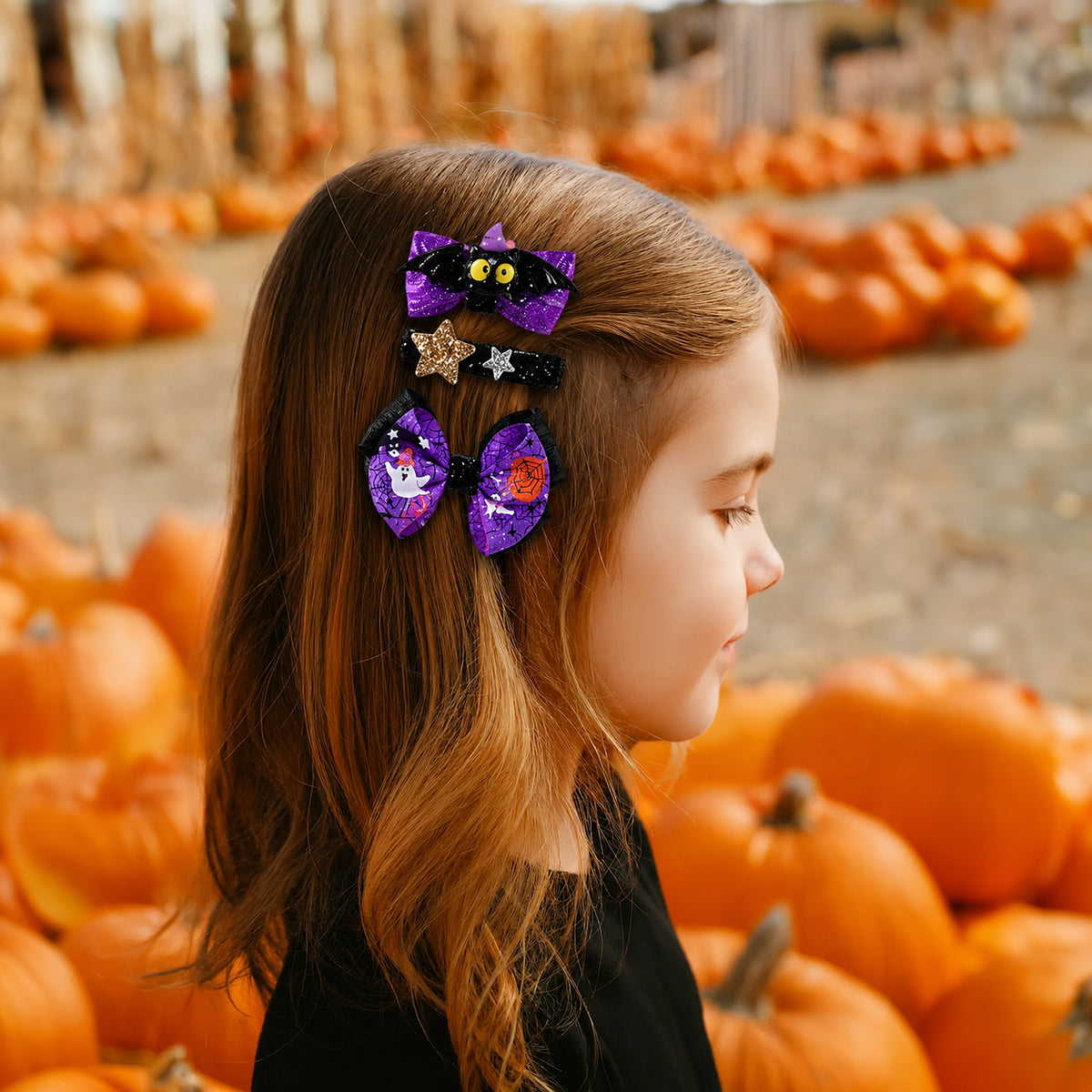 A young girl with long light brown hair is shown in profile wearing three purple Halloween-themed hair clips with black accents, set against a blurred pumpkin patch background.